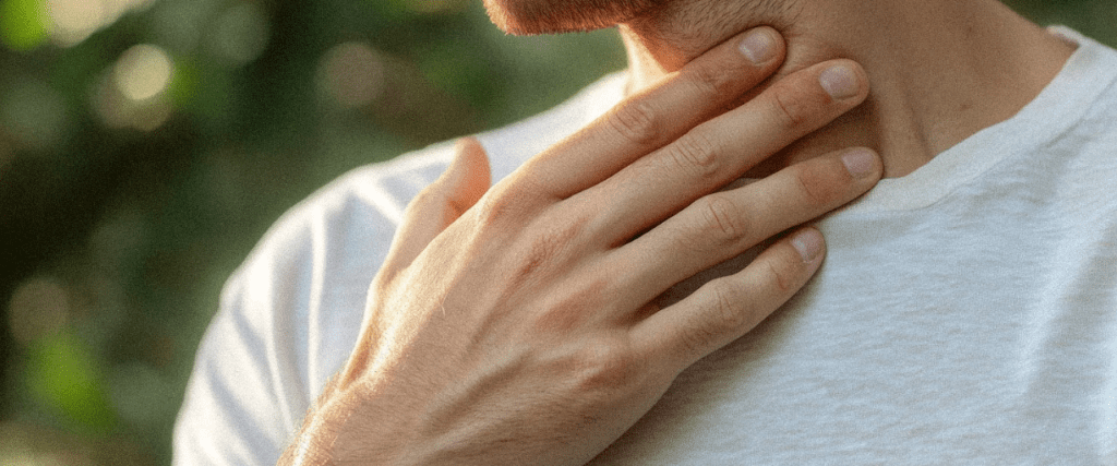 Homme caucasien vêtu d'un t-shirt gris touchant son cou où se trouve sa thyroïde.