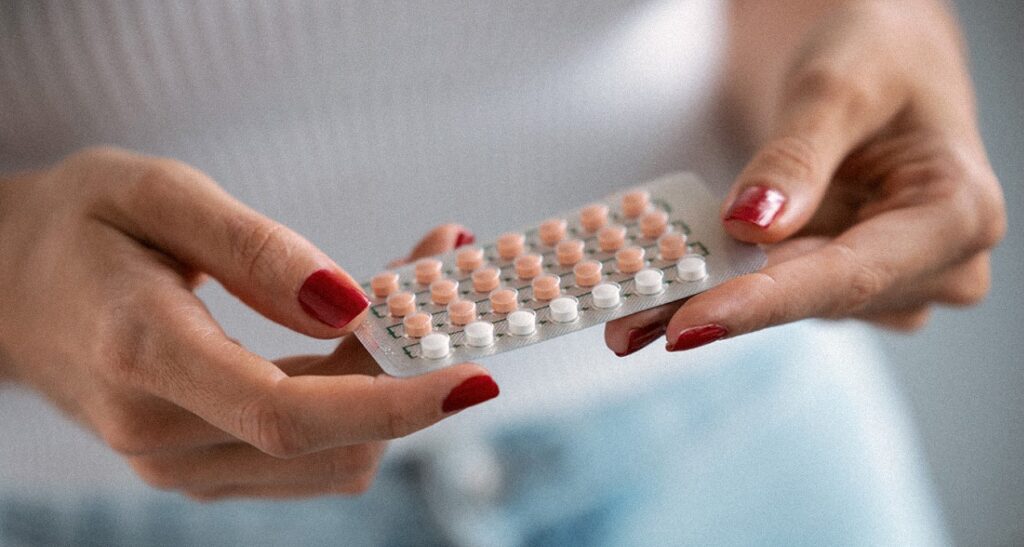 Femme aux ongles vernis de rouge tenant un emballage mensuel de pilules contraceptives.