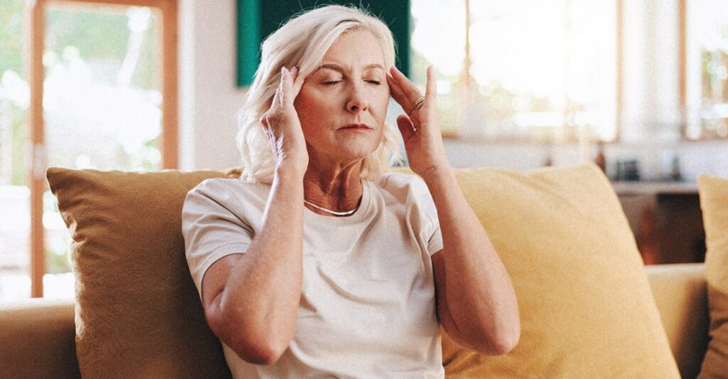 Older woman with her eyes closed, holding her temples, suffering from a tension headache due to high stress levels.