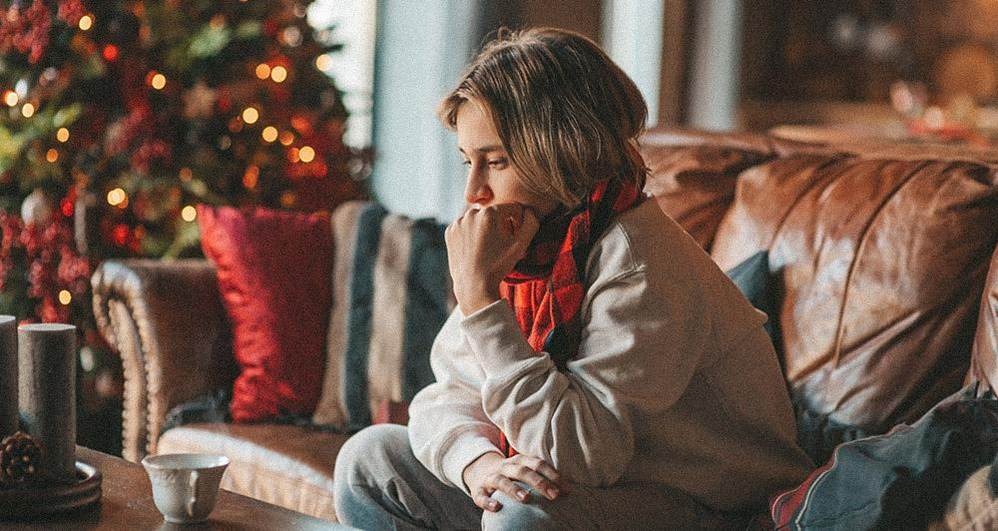 Une femme assise sur un canapé, entourée de décorations de vacances, semble triste. Elle évoque la solitude et le stress des vacances.