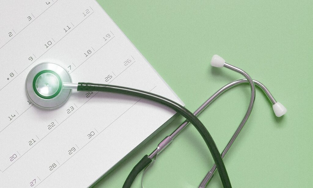 A calendar sitting on a blue background with a stethoscope on top to indicate an annual medical exam or check-up appointment.