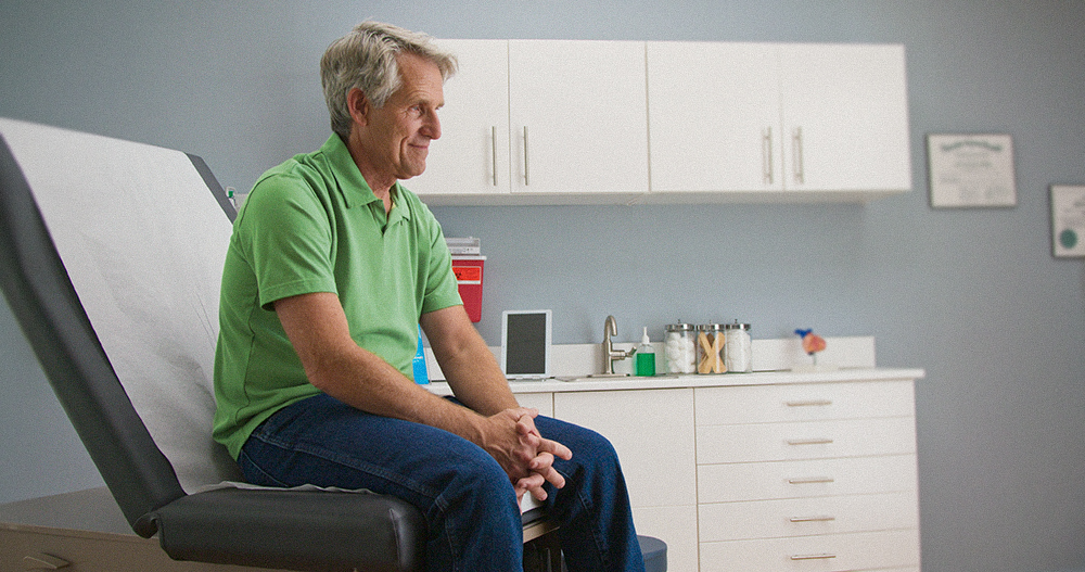 Senior caucasian male patient waiting for the doctor at an annual check-up, sitting on an exam room table