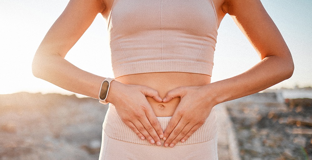 Close-up of a woman making the shape of a heart with her hands over her uterus.