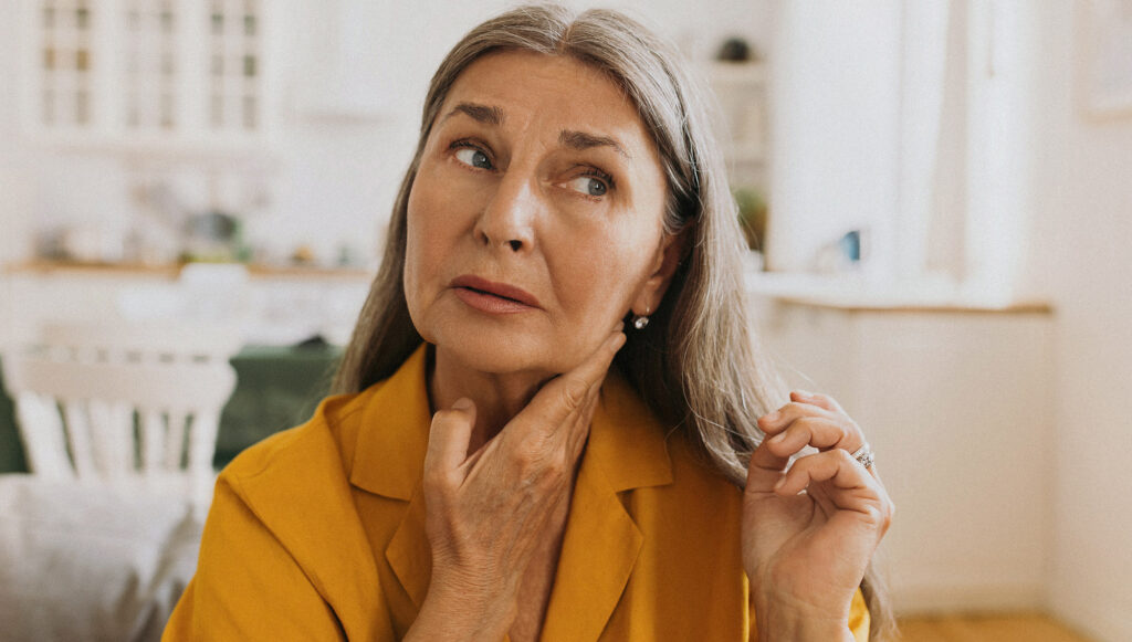 Elderly woman feeling pain in her neck, swollen thyroid.